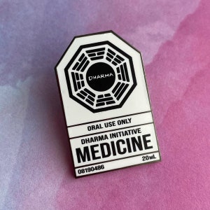 Puede incluir: Un pin de esmalte blanco y negro con el logotipo de Dharma Initiative. El pin dice "ORAL USE ONLY", "DHARMA INITIATIVE" y "MEDICINE", con "20ml" y el número "08190486". El pin está sobre un fondo rosa y morado.