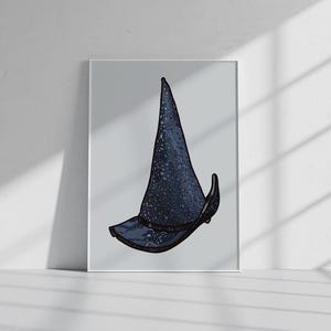 May include: A framed art print featuring a dark blue, speckled, pointed hat with a wide brim and a black band around the base. The illustration has a textured, starry appearance and is centred within a simple white frame on a light background.