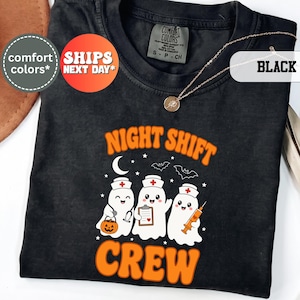 May include: A black t-shirt featuring a graphic of three ghost nurses with the text "NIGHT SHIFT CREW" in orange. The ghosts wear nurse caps and hold a pumpkin bucket, a clipboard, and a syringe. The design includes stars, bats, and a moon.
