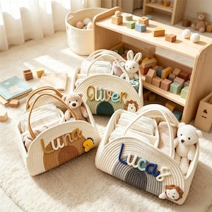Puede incluir: Tres cestas de almacenamiento de cuerda tejida en color blanco roto con asas, cada una con un diseño de arcoíris y un nombre personalizado en letras de tela en relieve: Luna en marrón, Oliver en verde y Lucas en azul, con peluches.