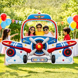 May include: A large, colourful aeroplane-shaped photo booth prop featuring a blue, red, and white design with a central propeller, landing gear, and clouds. The front displays the text READY FOR FUN! in a rectangular frame with a star emblem above.
