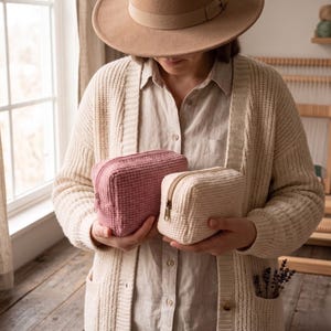 May include: Two rectangular zippered pouches with a textured waffle-knit fabric pattern. One pouch is a dusty rose pink color, and the other is a cream off-white color. Both pouches feature a matching zipper closure along the top edge.