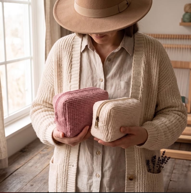 May include: Two rectangular zippered pouches with a textured waffle-knit fabric pattern. One pouch is a dusty rose pink color, and the other is a cream off-white color. Both pouches feature a matching zipper closure along the top edge.