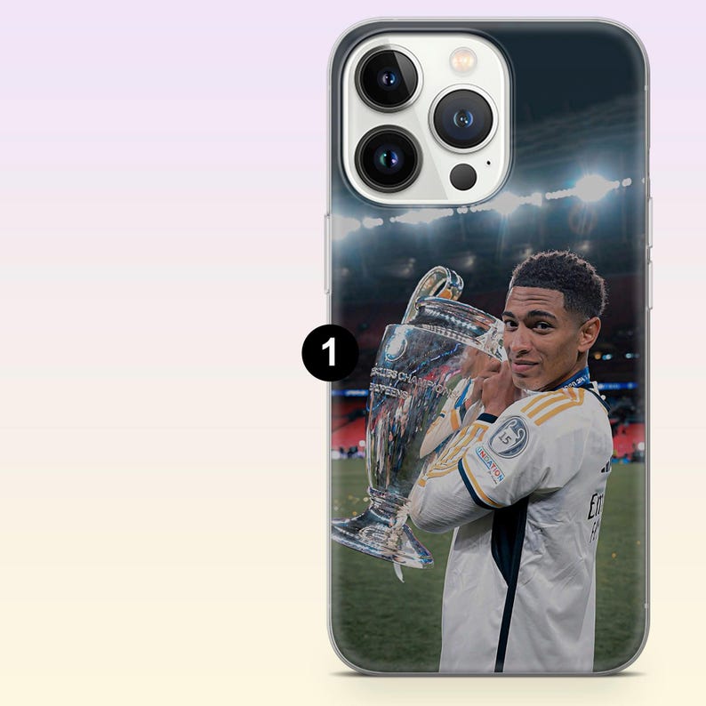 May include: A clear smartphone case featuring a printed image of a soccer player in a white jersey holding a large silver trophy on a field. The design includes the player looking over their shoulder with the stadium lights visible in the background.