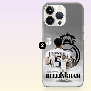 May include: A smartphone case featuring a graphic of Jude Bellingham in a white Real Madrid kit. The design includes the number 5, the Real Madrid crest, and the text 'REAL MADRID BELLINGHAM' in black and white tones on a grey background.
