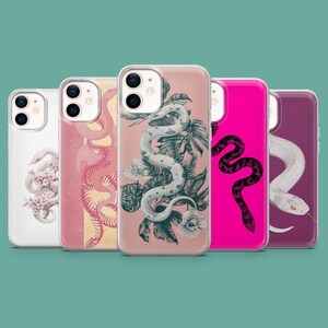 Puede incluir: Cinco fundas para smartphone dispuestas en fila, cada una con una ilustración de serpiente única. Los diseños incluyen una serpiente blanca con flores rosas, un esqueleto de serpiente rosa, una serpiente blanca entre hojas y una negra.