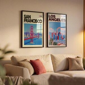 May include: Two framed vertical wall art prints featuring cityscapes. The left print displays the Golden Gate Bridge with the text San Francisco. The right print shows the Los Angeles skyline with mountains and the text Los Angeles in black font.
