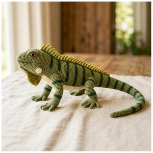 May include: A crocheted iguana toy featuring a textured green body with darker green vertical stripes, a cream-colored underbelly, a spiky dorsal crest along the back, and a long tail. The creature has a detailed head with a round eye and a small ear patch.