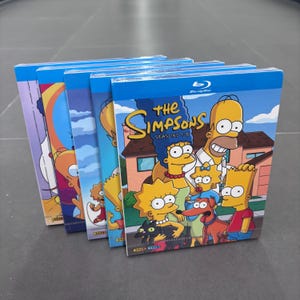 May include: A collection of The Simpsons Seasons 1-8 Blu-ray disc cases arranged in a row. The front cover features the Simpson family, including Homer, Marge, Bart, Lisa, and Maggie, along with their pets, standing in front of their suburban home.