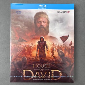 Może przedstawiać: Etui na płytę Blu-ray z drugim sezonem House of David, przedstawiające brodatego mężczyznę w koronie nad wojownikiem w zbroi na polu bitwy z żołnierzami, flagami i dymem. Tytuł znajduje się na dole i jest napisany złotymi literami.