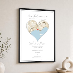Peut inclure: Une affiche encadrée présentant une carte en forme de cœur de Cannes, France, avec un marqueur rouge. Le texte indique "Là où tout a commencé," "Victoria & Kévin," "Cannes, France," des coordonnées et la date "27 Juin 2026" en noir.