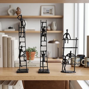 Pode incluir: Três esculturas de metal preto representando figuras humanas abstratas interagindo com escadas. A primeira mostra duas figuras a subir, a segunda mostra duas figuras a subir e a terceira mostra três figuras sentadas ou de pé nos degraus.