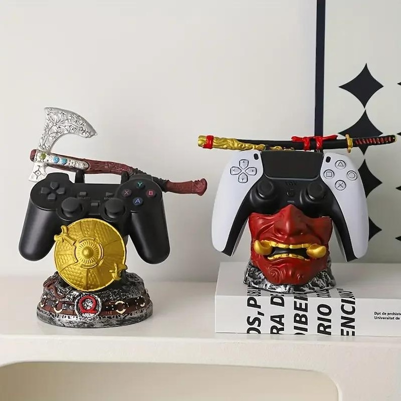 Peut inclure: Deux supports pour manettes de jeu. Le support de gauche pr&eacute;sente une hache argent&eacute;e et un bouclier dor&eacute; tenant une manette noire. Le support de droite pr&eacute;sente un masque japonais rouge et un katana noir et dor&eacute; tenant une manette blanche et noire.