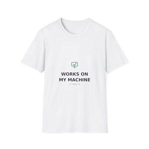 May include: A white short-sleeve t-shirt featuring a green computer monitor icon with a checkmark. Below the icon, the text reads "WORKS ON MY MACHINE" in black capital letters, followed by the smaller gray text "// ship it" underneath.