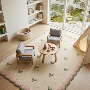 May include: A rectangular area rug featuring a cream-colored base with a repeating pattern of small green leaf motifs. The rug has a scalloped edge bordered by a pink band and a green outer trim, providing a soft texture for a floor space.