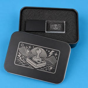 Könnte beinhalten: Eine schwarze, rechteckige Aufbewahrungsdose aus Metall mit einem Deckel, der eine weiße Strichzeichnung eines Retro-Joysticks, Gittermuster und Blitze zeigt. Im Inneren liegt ein schwarzer und transparenter Acryl-USB-Stick in Schaumstoff.