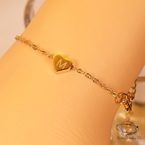 Peut inclure: Un bracelet à chaîne doré doté d'un petit pendentif central en forme de cœur gravé de la lettre M. Les maillons métalliques délicats sont reliés au cœur, qui constitue l'élément central de ce bijou simple et épuré.