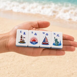 May include: Four white rectangular mahjong tiles featuring blue letters E, S, W, N and corresponding Japanese characters. The tiles display colorful illustrations of a lighthouse, a rising sun, a sailboat with American flag colors, and the Statue of Liberty.