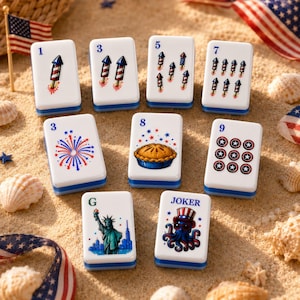 May include: A set of nine white rectangular mahjong tiles featuring patriotic American-themed illustrations. The tiles display fireworks, rockets, a pie, the Statue of Liberty, and a joker octopus, each marked with numbers or the letter G.