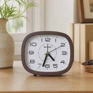 Puede incluir: Un reloj de mesa rectangular con esquinas redondeadas y un marco de madera de color marrón oscuro. La esfera blanca presenta números arábigos negros, manecillas negras para horas y minutos, un segundero fino y el texto Geremy Quartz en el centro.