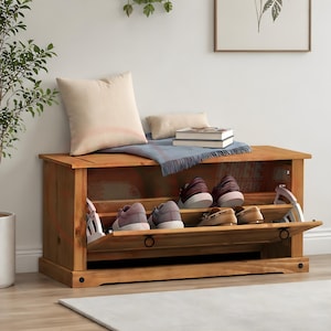 May include: A rectangular wooden shoe storage bench with a natural light brown finish. The unit features a drop-down door revealing interior shelving that holds four pairs of shoes. A beige pillow, a small cushion, and two books sit on top.