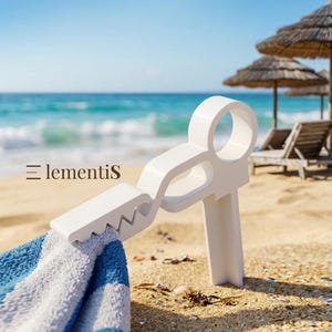 Op de afbeelding: Een witte plastic strandhanddoekklem met een cirkelvormige handgreep en een gekarteld klemmechanisme, die een blauw-wit gestreepte handdoek vasthoudt. De tekst "Elementis" is in het zwart gedrukt op de bovenarm van de klem.