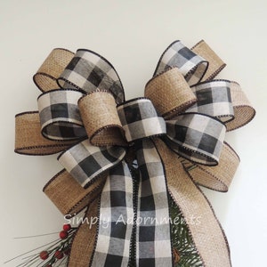 May include: A black and white buffalo plaid ribbon bow with burlap ribbon tails and a sprig of greenery with red berries. "Simply Adornments" is written on the burlap ribbon.