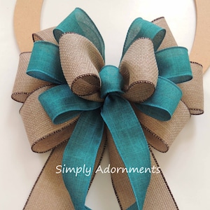 May include: A teal and brown burlap bow with a brown edge. The bow is tied with two long tails, one teal and one brown. The text "Simply Adornments" is visible on the bow.