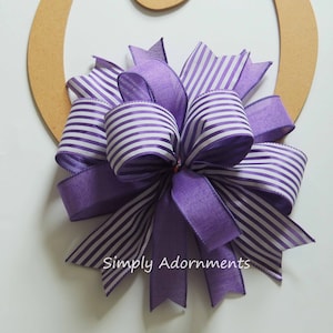 May include: A purple and white striped ribbon bow with a purple bow in the center, attached to a wooden letter O.