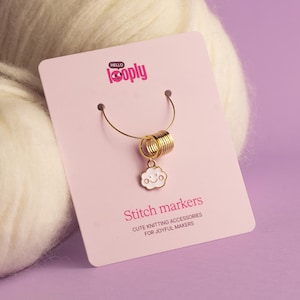 Può includere: Un segnapunti in metallo color oro con un ciondolo a forma di nuvola bianca con un viso sorridente, attaccato a un anello a spirale. L'articolo è mostrato su un cartoncino rosa chiaro con il testo Hello Looply, Stitch markers e CUTE KNITTING ACCESSORIES FOR JOYFUL MAKERS.