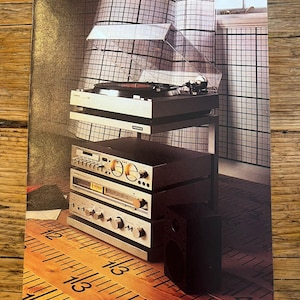 Peut inclure: Une publicité vintage pour un système audio Pioneer avec une platine, une platine cassette, un tuner et un amplificateur empilés sur un support en métal. Le texte indique : amplifier, the TX-3000 tuner, the CT-3000 cassette deck and the PL-3000 turntable, linked with full literature. PIONEER EVERYTHING YOU HEAR IS TRUE.