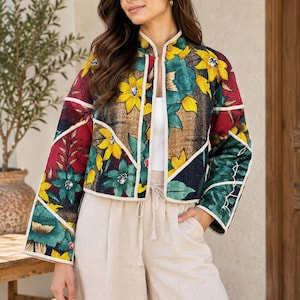 May include: A cropped, long-sleeve jacket featuring a vibrant patchwork design of yellow sunflowers and teal floral patterns on a dark background. The jacket has a mandarin collar, white piping trim, and a quilted texture throughout the fabric.