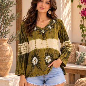 May include: A long-sleeve V-neck top featuring an olive green and cream tie-dye pattern with circular sunburst motifs and thin black line details, paired with light blue denim shorts that have a frayed hemline and a classic five-pocket design.