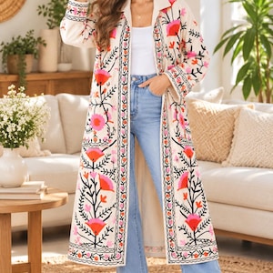 May include: A long, cream-colored open-front duster coat featuring vibrant floral embroidery in shades of pink, orange, and black. The garment has long sleeves, a collared neckline, and a straight hem that falls below the knees.