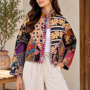 May include: A cropped jacket featuring a patchwork design with various floral and geometric patterns in shades of black, yellow, orange, and blue. The jacket has a high collar, long sleeves, and a white trim along the front opening and cuffs.