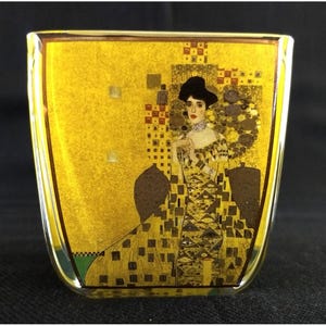 May include: A square glass vase featuring a vibrant gold-toned print of Gustav Klimt's Portrait of Adele Bloch-Bauer I. The design displays a figure in a patterned gown with geometric shapes, dark brown accents, and a bright yellow background.
