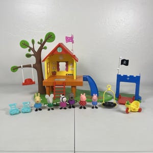 Op de afbeelding: Een Peppa Pig boomhut speelset met een geel huis met een rood dak, een bruine boom met een rode schommel, een blauwe glijbaan en een blauwe kasteelpoort met een zwarte piratenvlag. Inclusief zes kleine dierenfiguren, twee lichtblauwe stoelen en een gele driewieler.