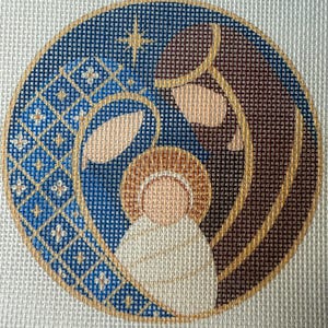 Könnte beinhalten: Ein kreisförmiges Stickbild mit einer stilisierten Krippenszene. Das Design umfasst einen blauen, gemusterten Bereich mit kleinen weißen Sternen, eine braune Figur und eine zentrale, in Weiß gehüllte Figur mit goldenem Heiligenschein, alles gold umrandet.