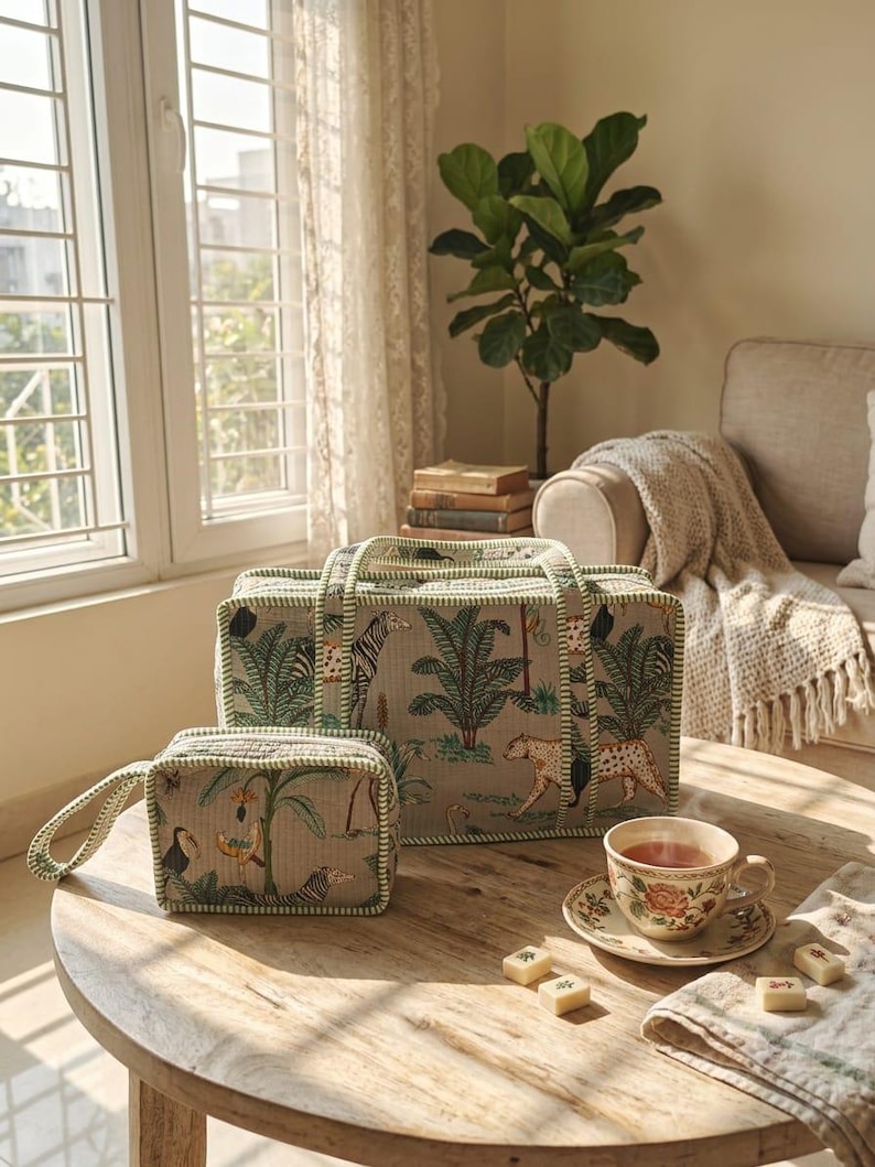 Puede incluir: Una bolsa de viaje rectangular y un neceser a juego, ambos de tela beige con un estampado de selva en verde y marr&oacute;n con animales y palmeras, rematados con ribetes a rayas verdes y blancas en los bordes y las asas.