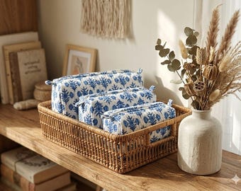 May include: Three rectangular quilted pouches with a blue floral block print pattern on a white background, arranged in a descending size order inside a rectangular woven rattan basket with side handles and a sturdy open-weave construction.