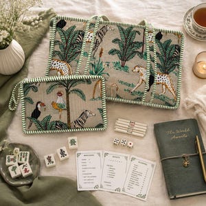 Puede incluir: Un bolso tote rectangular y un estuche con cremallera a juego, ambos de tela beige con un estampado de selva verde con leopardos, cebras y palmeras. El conjunto incluye fichas de mahjong blancas, dados, tarjetas de puntuaci&oacute;n y un diario.
