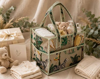 May include: A rectangular fabric storage caddy with two handles and a jungle animal print featuring zebras, giraffes, and tropical foliage on a beige background. The caddy has internal dividers and contains white diapers, bottles, and a teddy bear.