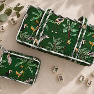 May include: A rectangular green storage case and a smaller matching rectangular pouch, both featuring a tropical jungle print with birds and zebras, finished with black and white striped piping trim and matching fabric handles.