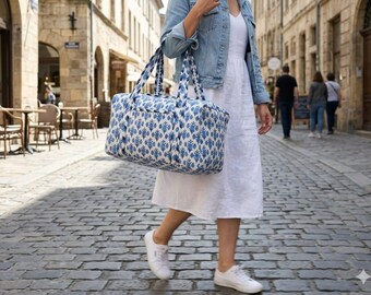 May include: A rectangular duffel bag featuring a blue and white botanical print pattern. The bag has two sturdy fabric handles and a zippered top closure. It is constructed from a quilted textile material with a repeating floral motif design.