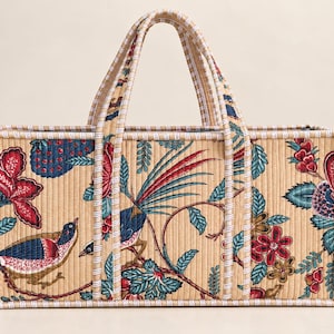 May include: A rectangular quilted tote bag featuring a beige background with a repeating pattern of colourful birds, red flowers, and blue foliage. The bag has two matching handles and is finished with a white and blue striped fabric trim.