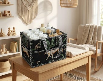 May include: A black fabric storage caddy featuring a repeating pattern of leopards and green palm leaves. The rectangular organizer has black and white striped handles and trim, with internal dividers holding white rolled cloths and bottles.