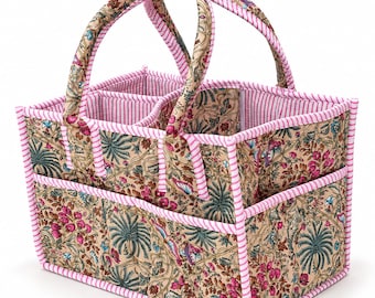 May include: A rectangular fabric storage caddy featuring a beige base with a floral pattern in shades of pink, green, and blue. The organizer includes two padded handles and exterior pockets, all finished with pink and white striped fabric trim.