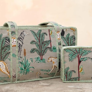 Puede incluir: Un bolso tote rectangular y un neceser rectangular m&aacute;s peque&ntilde;o a juego, ambos de tela gris claro con un estampado de selva de cebras, leopardos, tucanes y palmeras, rematados con ribetes de tela a rayas verdes y blancas.
