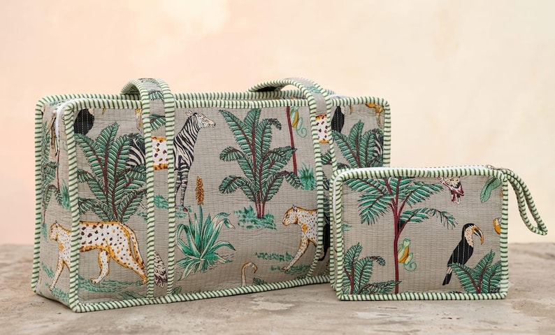 Puede incluir: Un bolso tote rectangular y un neceser rectangular m&aacute;s peque&ntilde;o a juego, ambos de tela gris claro con un estampado de selva de cebras, leopardos, tucanes y palmeras, rematados con ribetes de tela a rayas verdes y blancas.