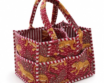 May include: A quilted fabric storage caddy featuring a red background with a repeating yellow and black leopard print pattern. The rectangular organizer has two sturdy handles, multiple exterior pockets, and a red and white striped trim.